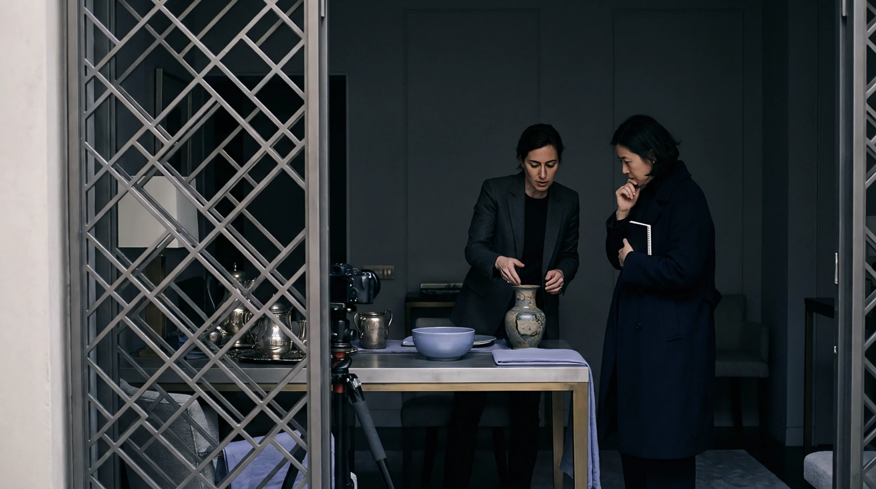 Two quality control specialists meticulously inspect a ceramic vessel on a work table for product compliance and condition documentation.