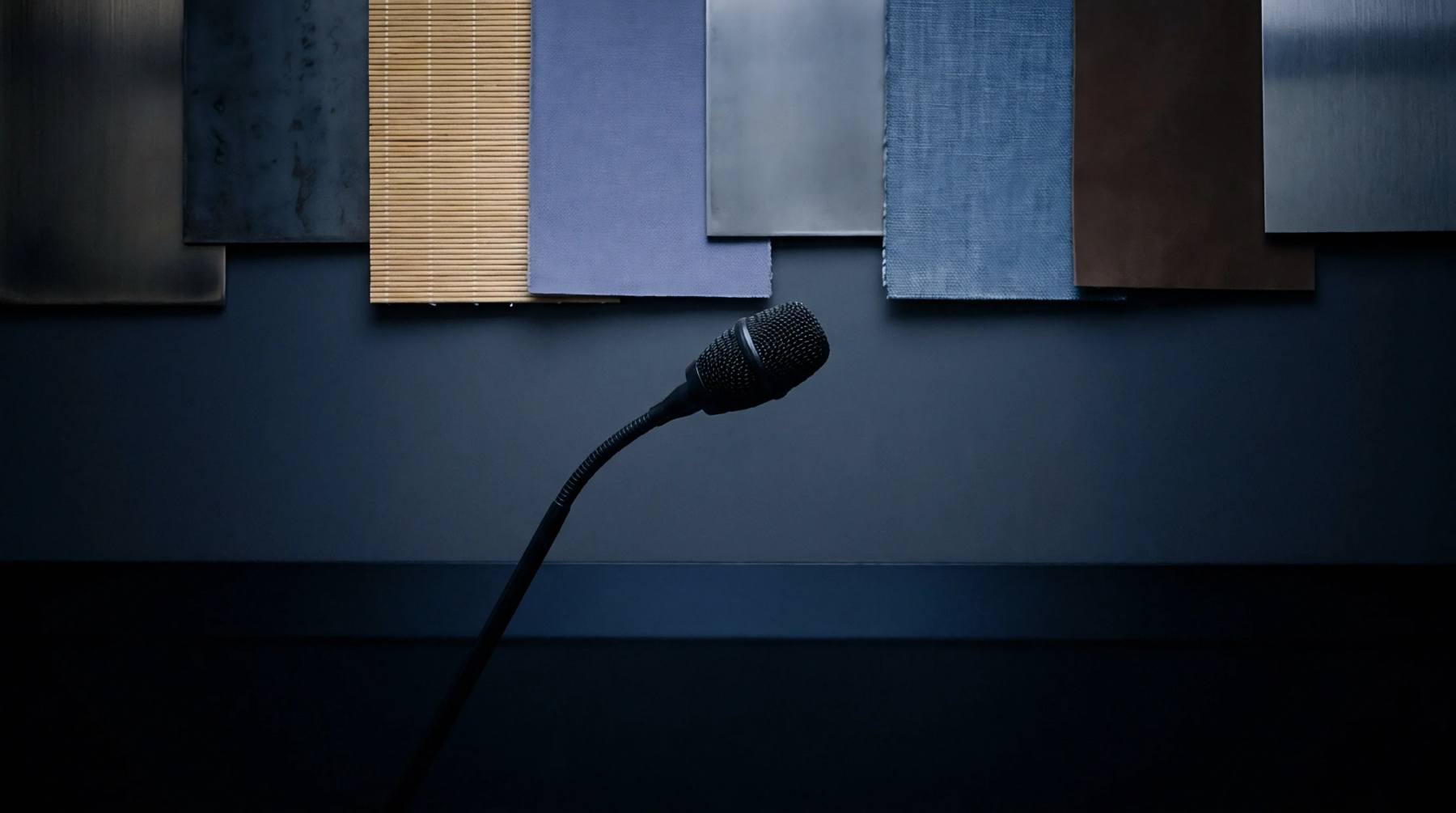 Various industrial material panels hang above a conference microphone positioned on a dark workbench inside a development facility.