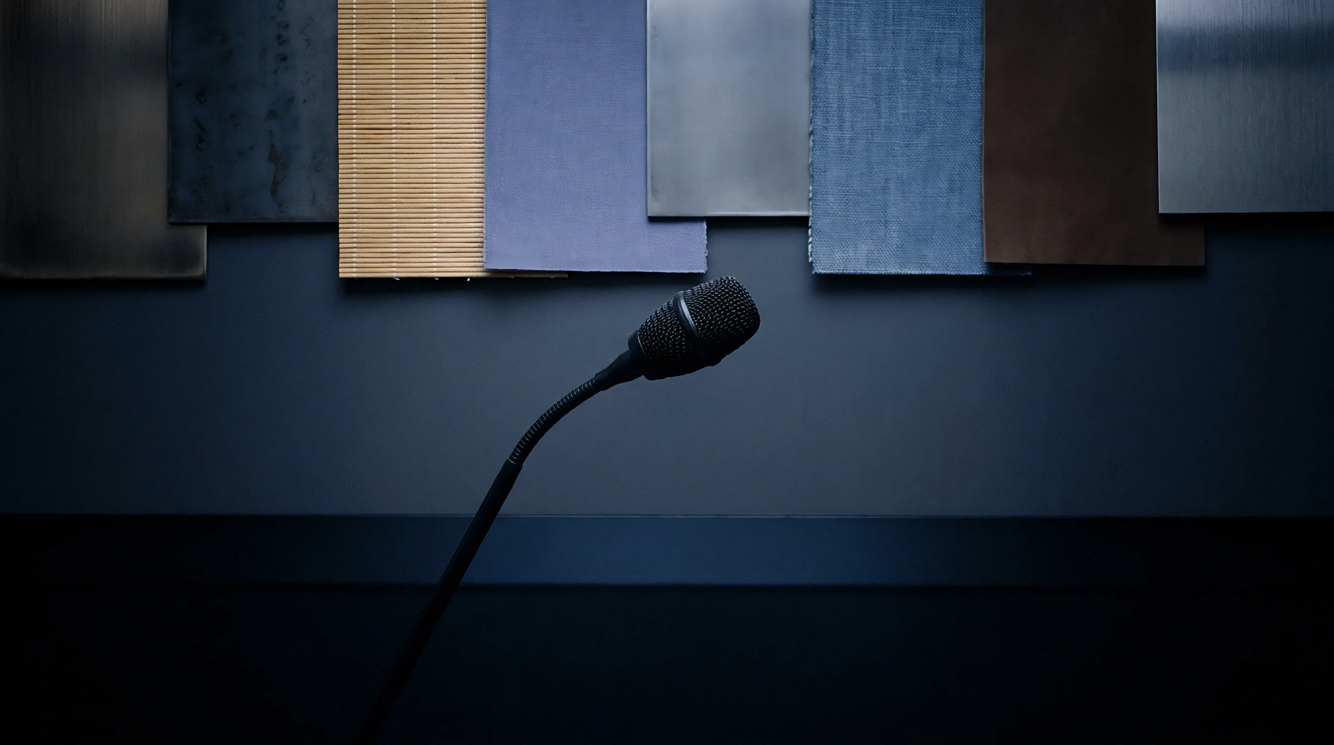 Various industrial material panels hang above a conference microphone positioned on a dark workbench inside a development facility.