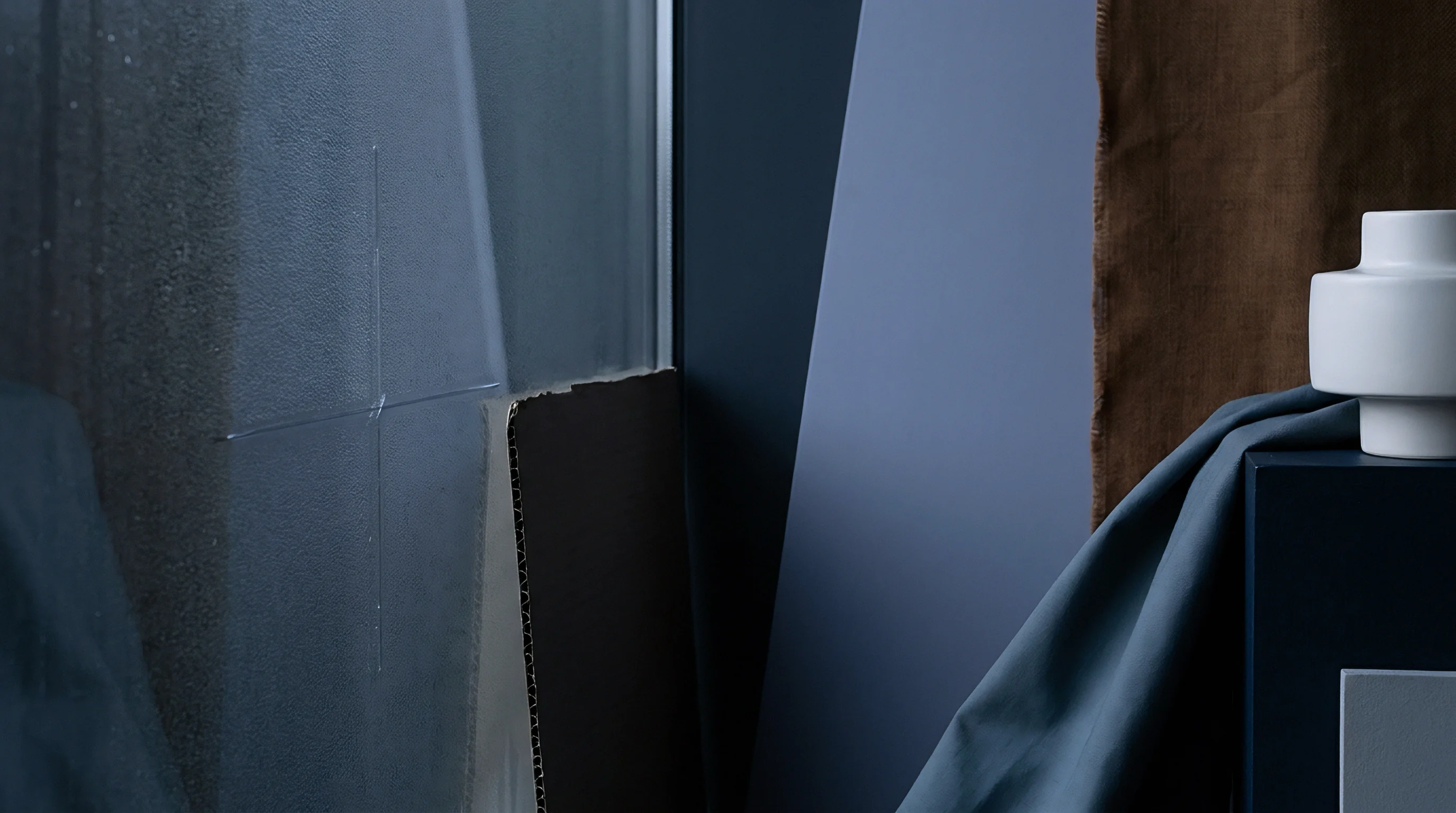 Architectural material samples featuring textured panels and fabric swatches are displayed beside a minimalist ceramic vessel in a production studio.